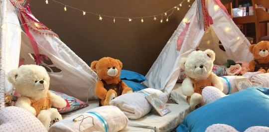 Camitas con mantas, cojines azules y peluches bajo tipis decorados con luces