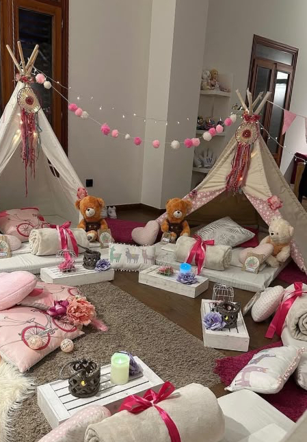 Dos tipis decorados con cuatro camitas, cojines rosas, peluches y luces, preparados en un salón